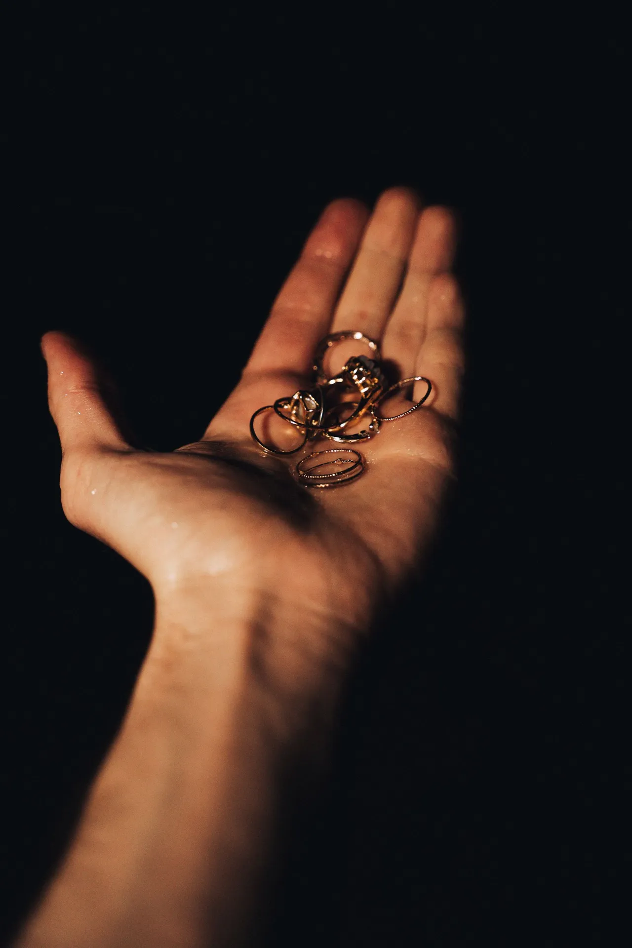 A hand holding a personal collection of rings, lit against a deep black background